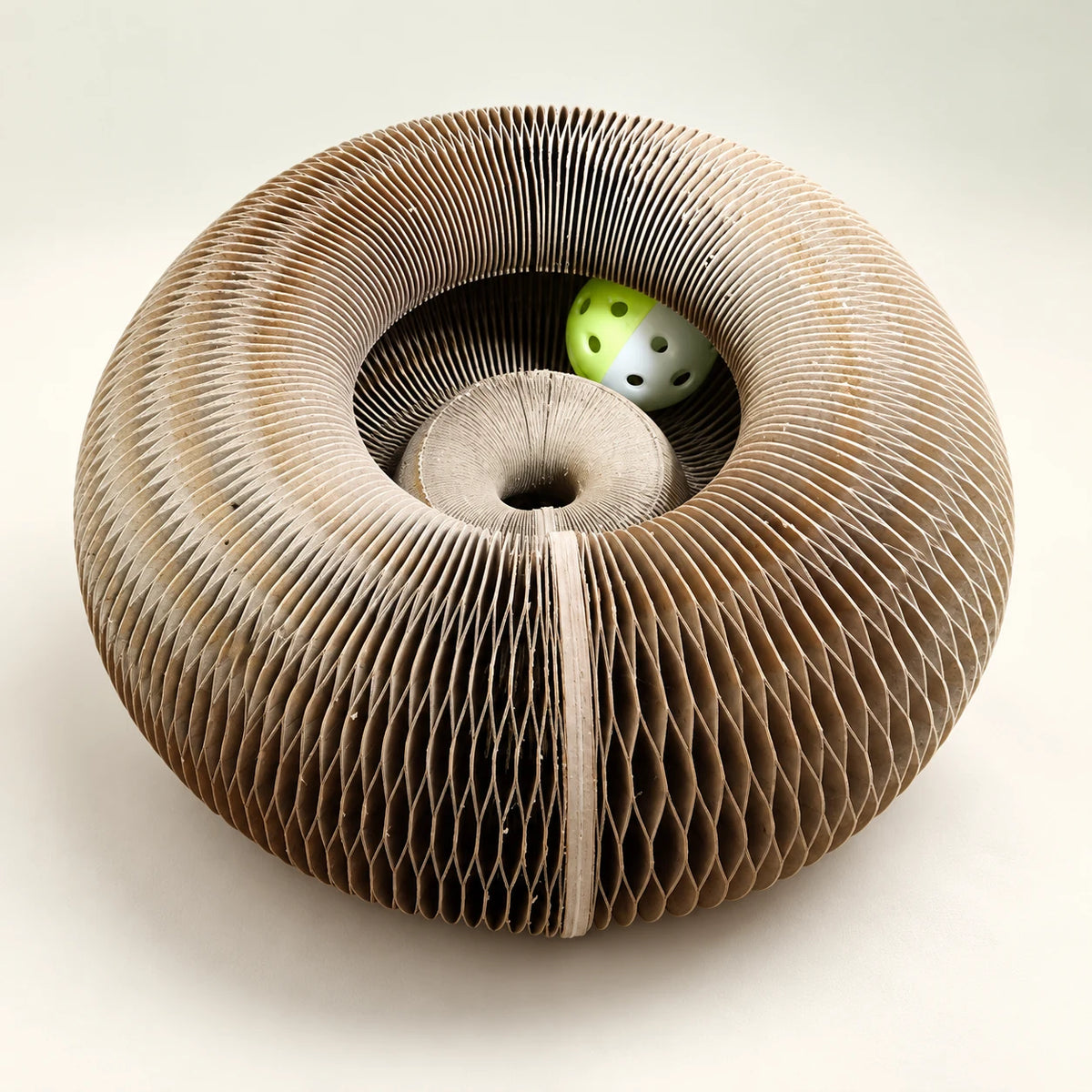 CurlNest accordion paper cat scratcher in a circular shape with its green-and-white play ball.
